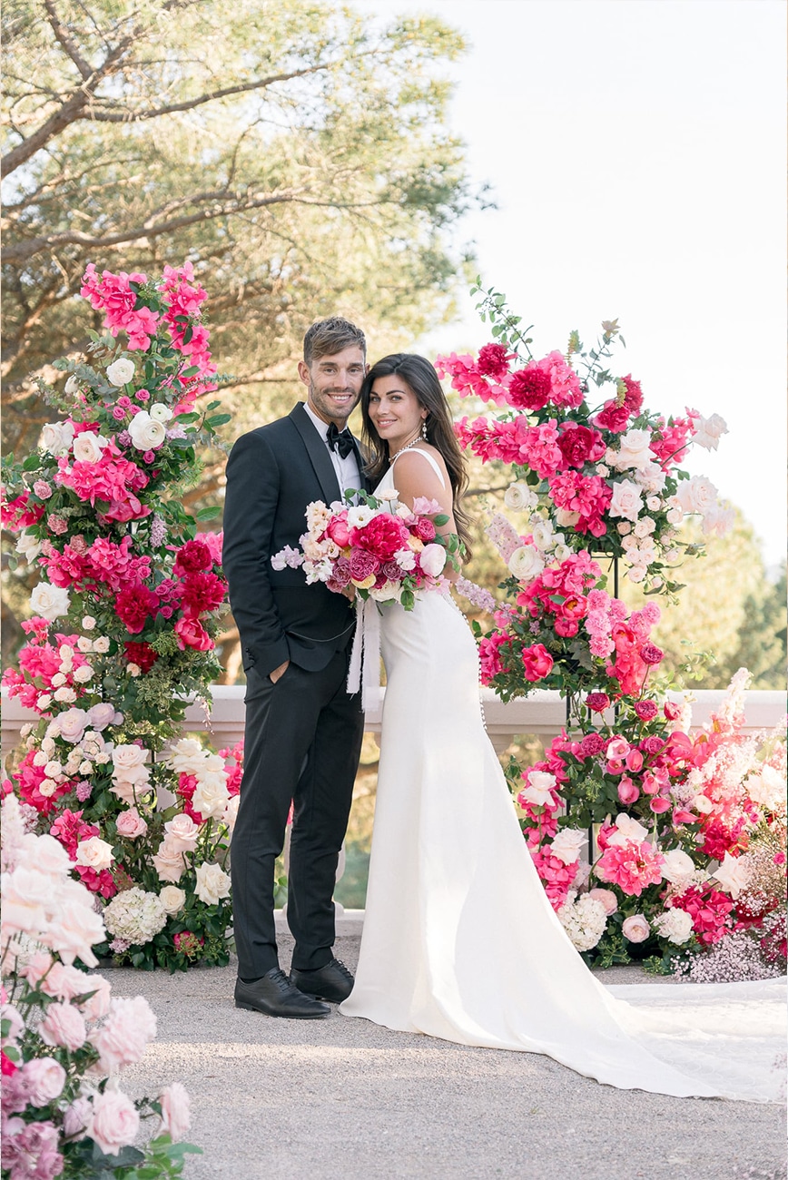 Couple in front of a fushia and pink wedding arch in Castel Bay