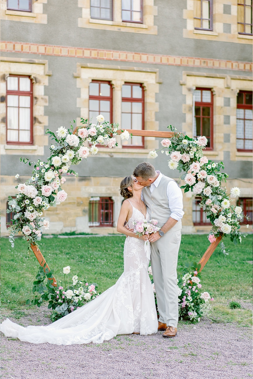 Bride and groom kissing in front of a pastel wedding arch