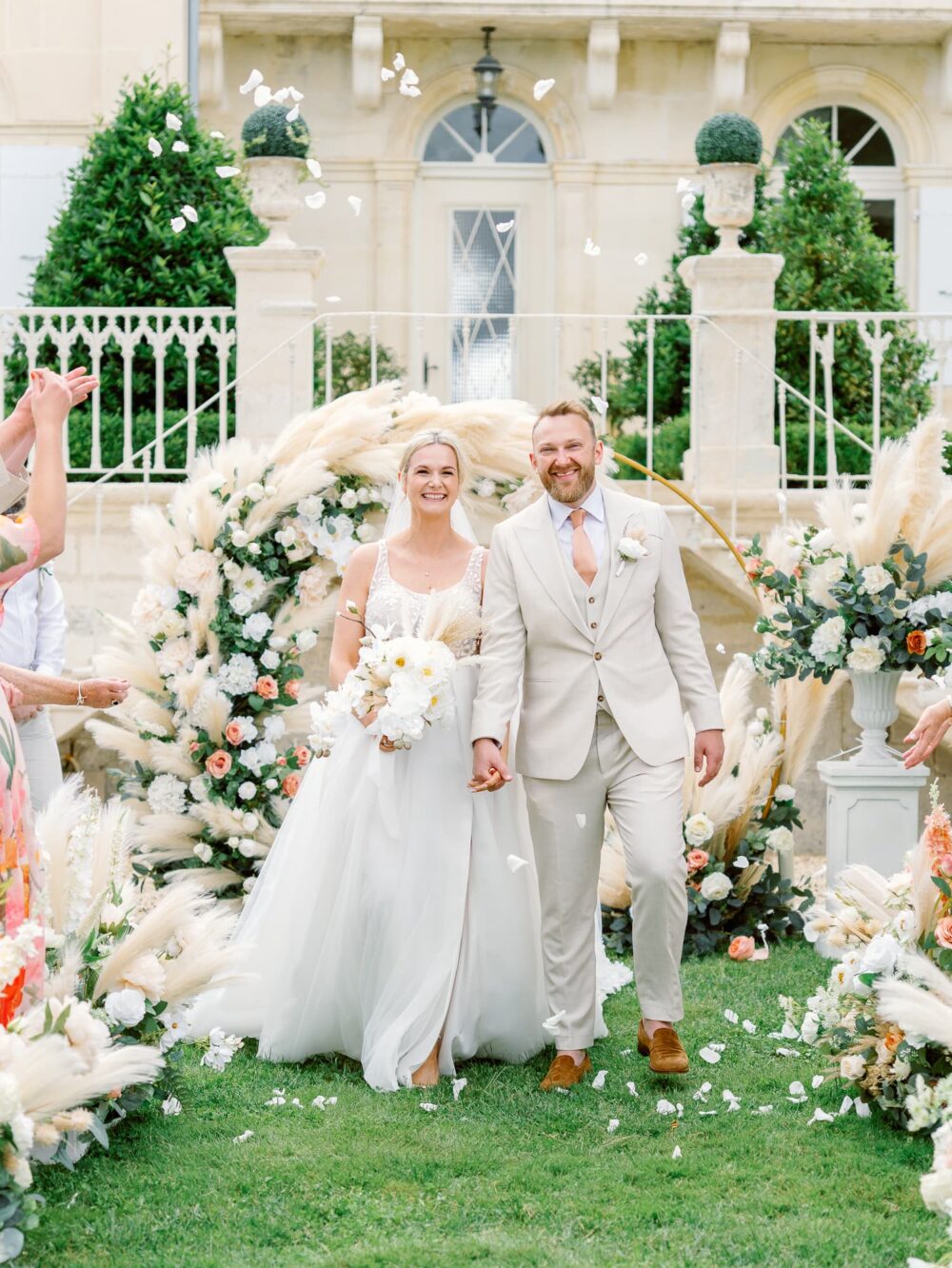 The bride and groom leaving the ceremony while the guests throw white petals, at Château N°3