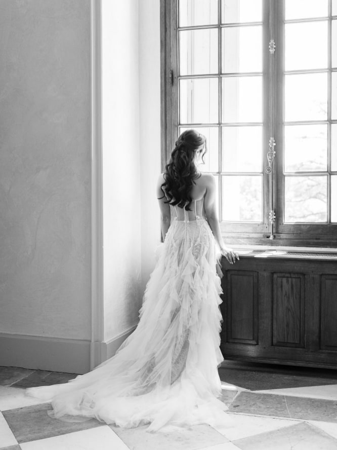 Bride standing at the window of a french chateau wearing a white dress