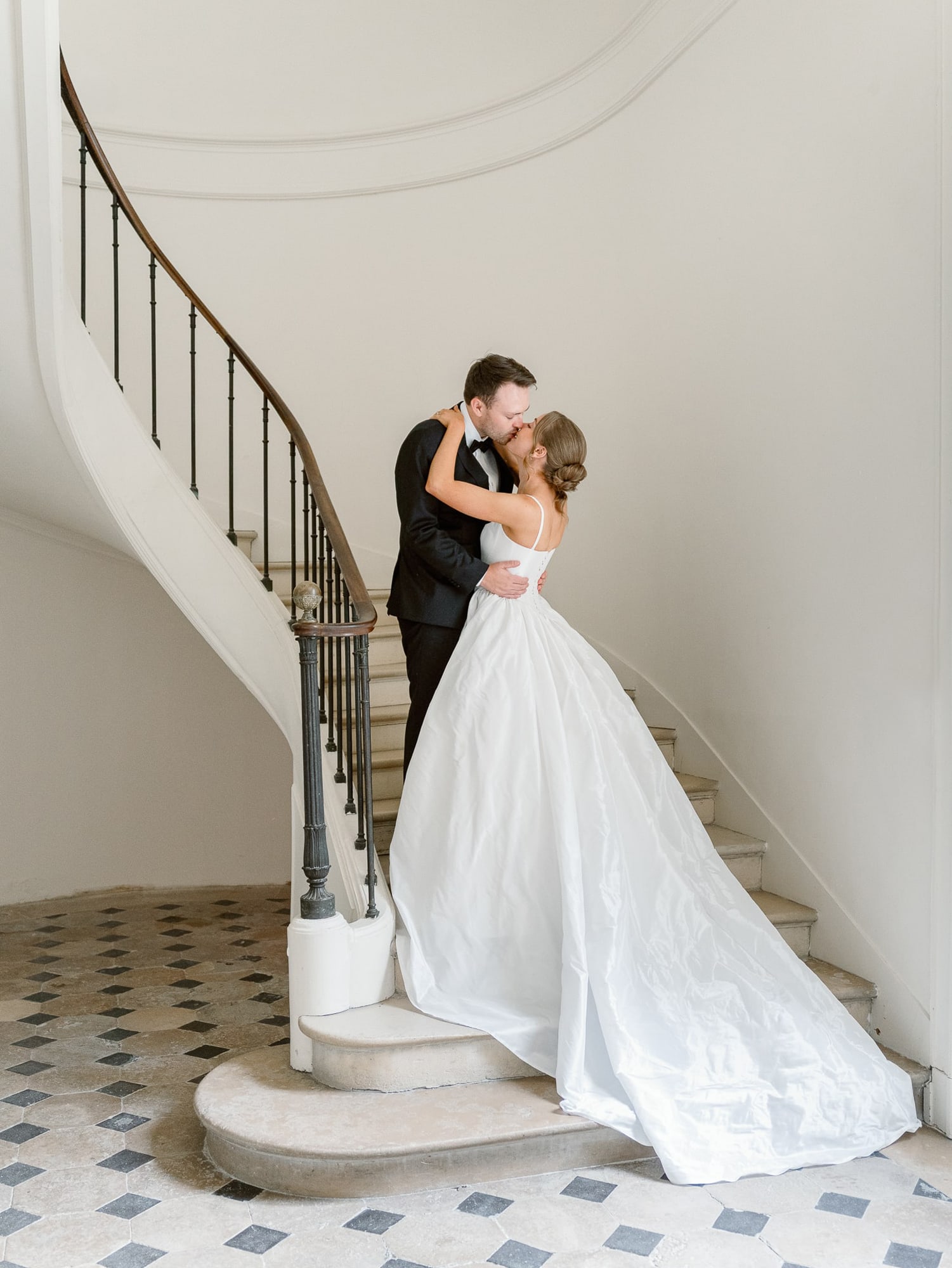 Elegant bride and groom kissing in a chateau staircase. The groom is wearing a black suit and the Bride a long white dress