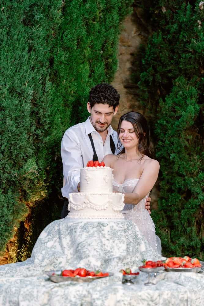 Couple cutting a white cake with red berries