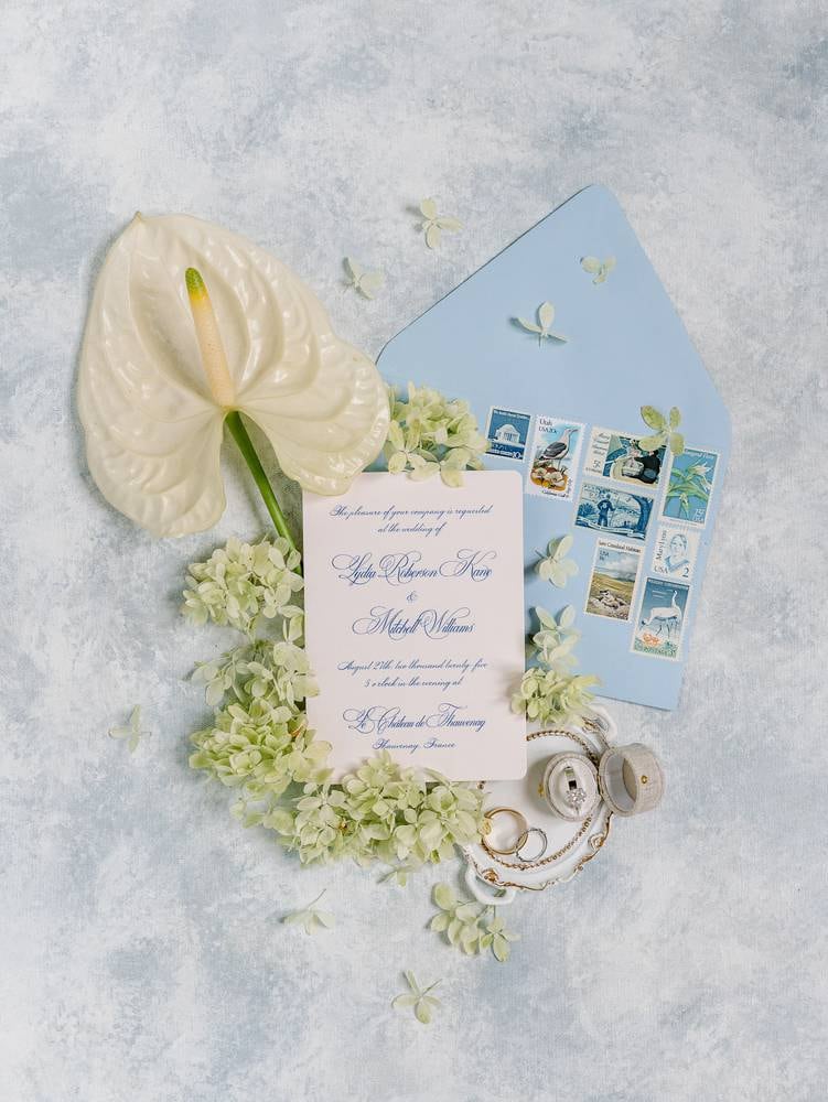 wedding flatlay of invitations with a blue enveloppe and an arum