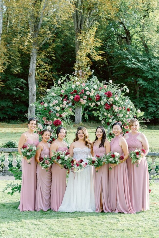 Bride and her bridesmaids in pink dresses holding bouquets with bordeau flowers and green foliage