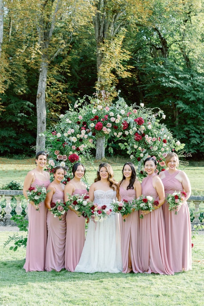 Bride and her bridesmaids in pink dresses holding bouquets with bordeau flowers and green foliage
