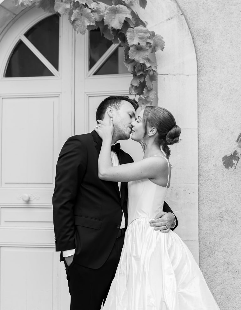 Couple de mariés s'embrassant devant une porte bordée de lierre