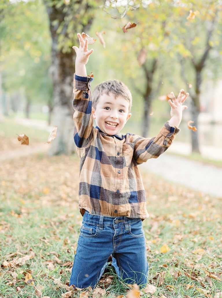 Enfant avec une chemise à carreaux lançant des feuilles en automne