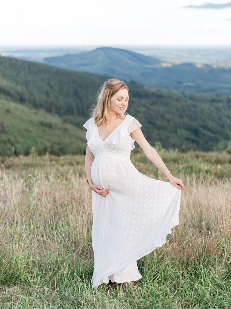 Femme enceinte en robe blanche dans la nature avec une vue sur collines et sapins