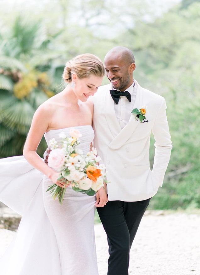 bride in a white dress with a bow, holding a spring bouquet and groom with a white suit