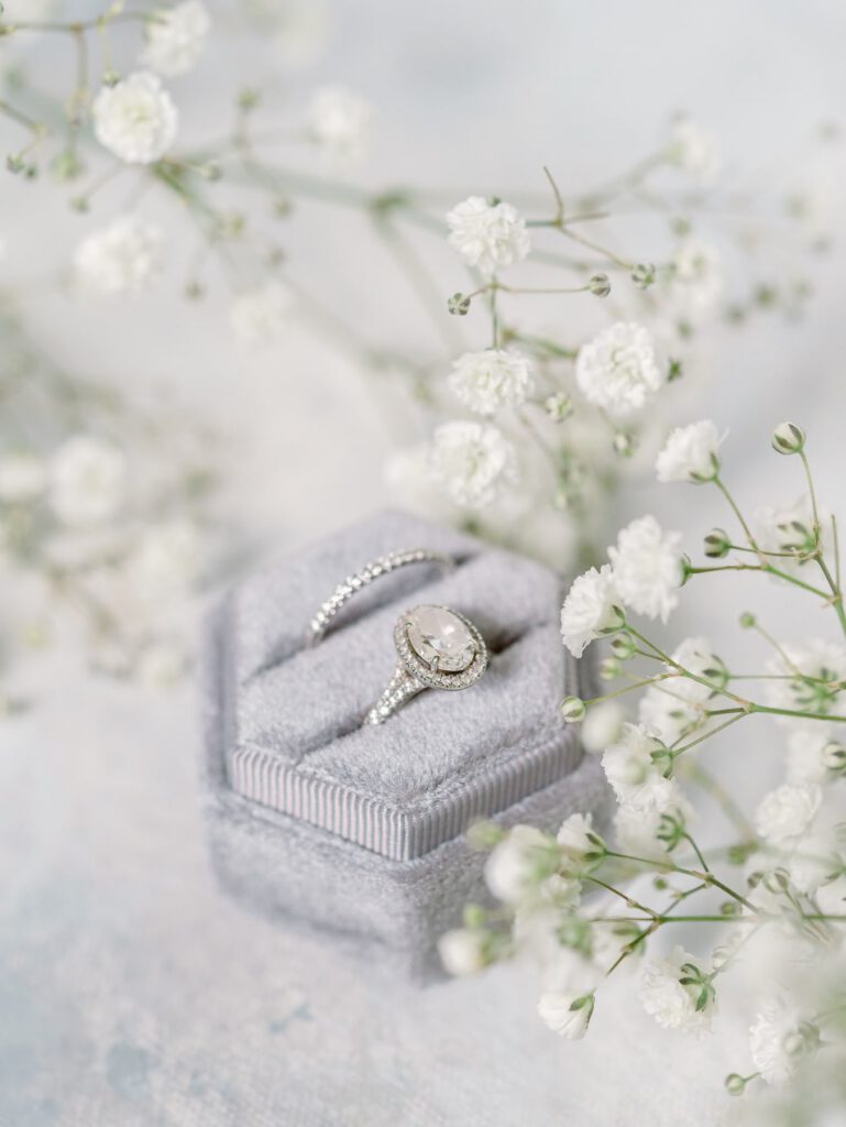 Grey ring box with silver rings in it, surrounded by white flowers