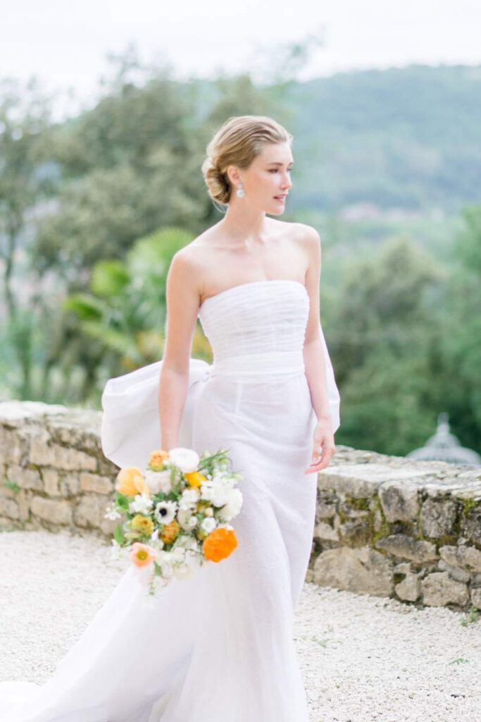 mariée avec une robe fine blanche et un bouquet à fleurs oranges et jaunes