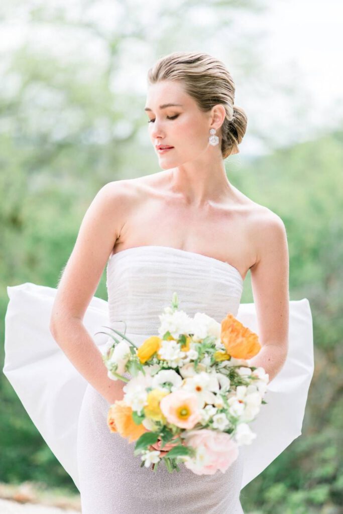 mariée avec une robe fine blanche et un bouquet à fleurs oranges et jaunes