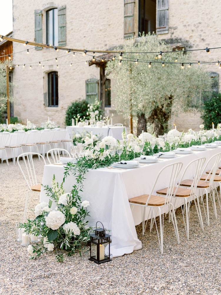 wedding reception with table with white tablecloth and white flowers, green foliage