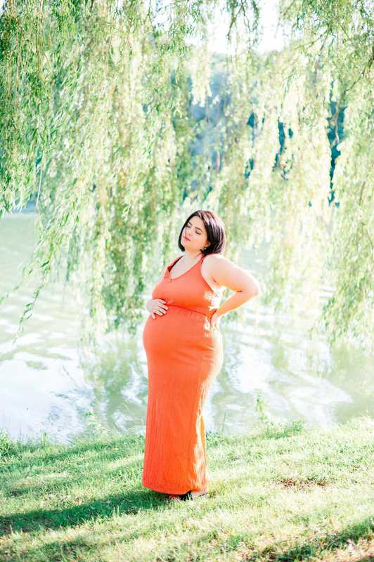 Femme enceinte en robe orange devant un lac et des arbres
