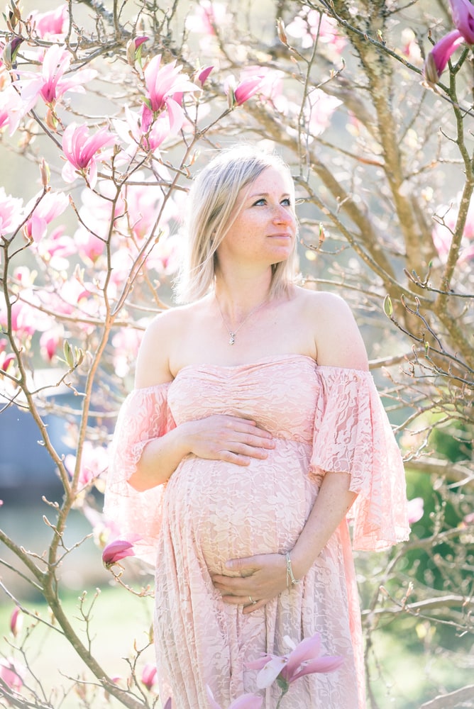 Femme enceinte en robe rose devant un magnolia en fleurs