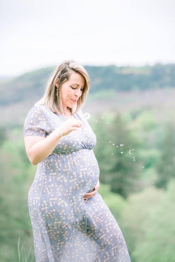 Femme enceinte en robe bleue soufflant sur un pissenlit