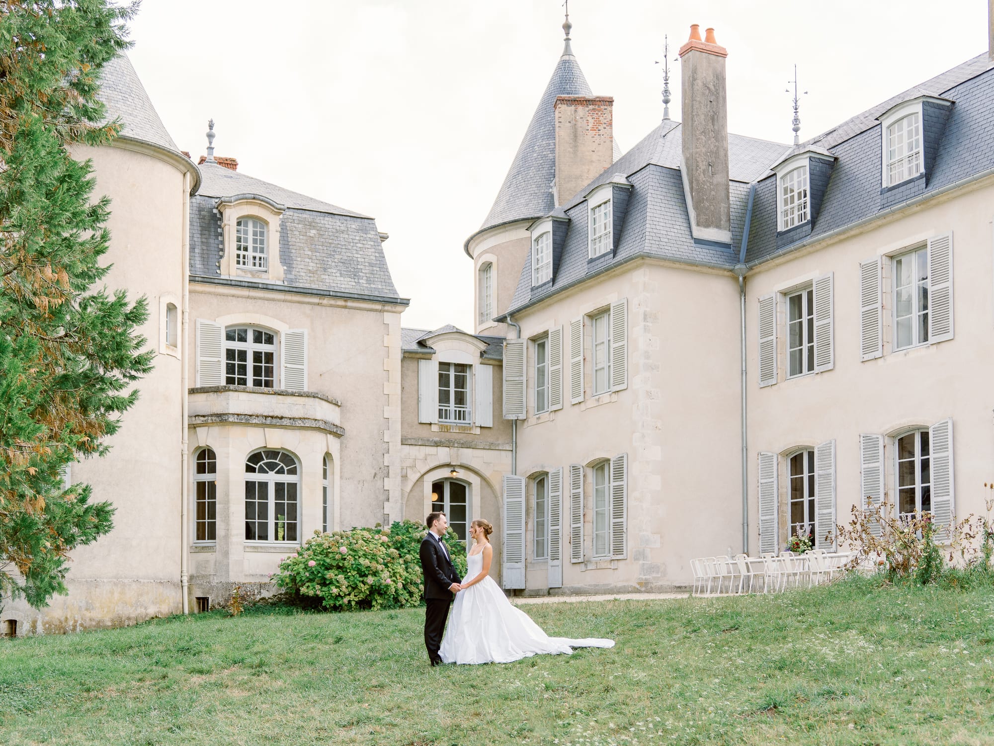 Bride and groom standing in front of Château de Thauvenay in France