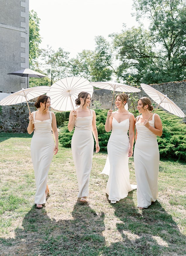 bride and her bridesmaids wearing champagne dresses walking laughing with parasols