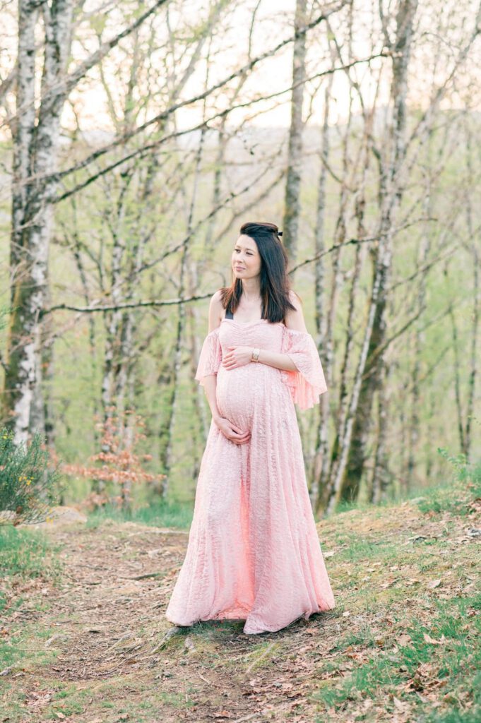 portrait d'une femme enceinte en robe rose dans une forêt au printemps