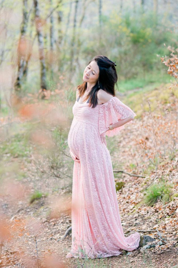 portrait d'une femme enceinte en robe rose dans une forêt au printemps