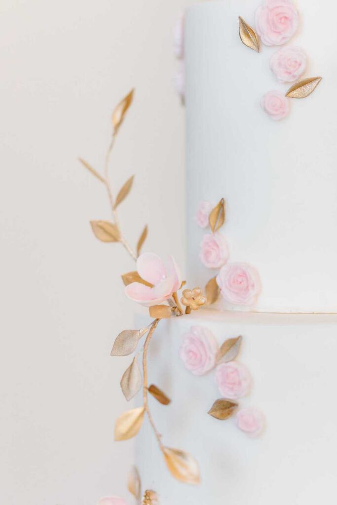 White wedding cake with golden leaves and pink flowers