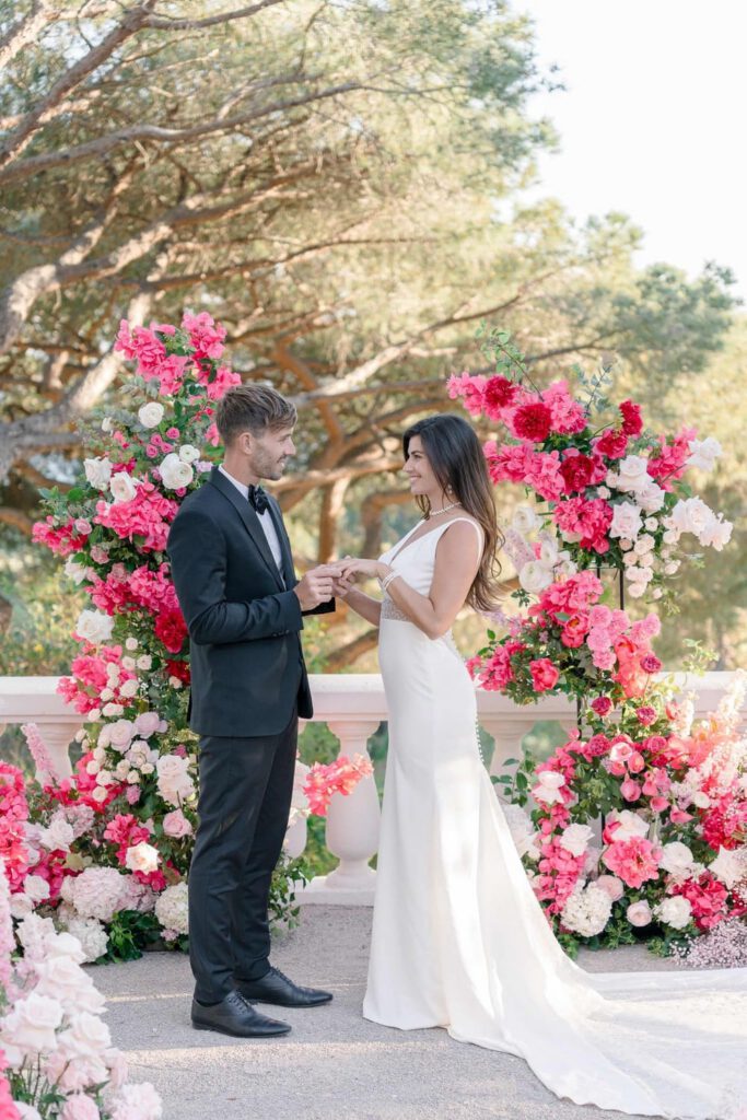 Wedding ceremony at castel bay with a big arch made with pink, magenta, fushia bold flowers