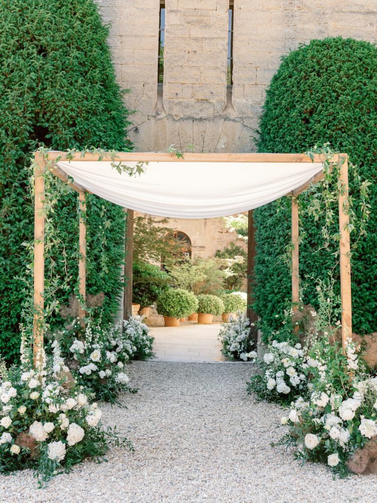 Wedding ceremony with a chuppah decorated with white flower and green foliage at Château de Fontarèches