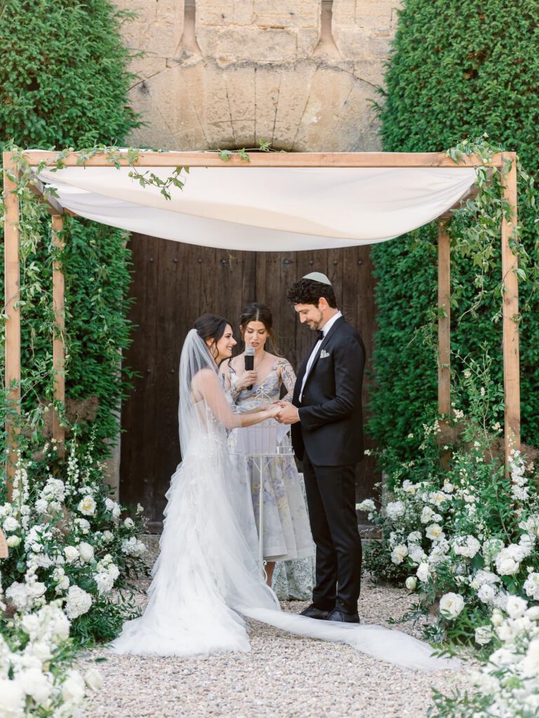Wedding ceremony with a chuppah decorated with white flower and green foliage at Château de Fontarèches