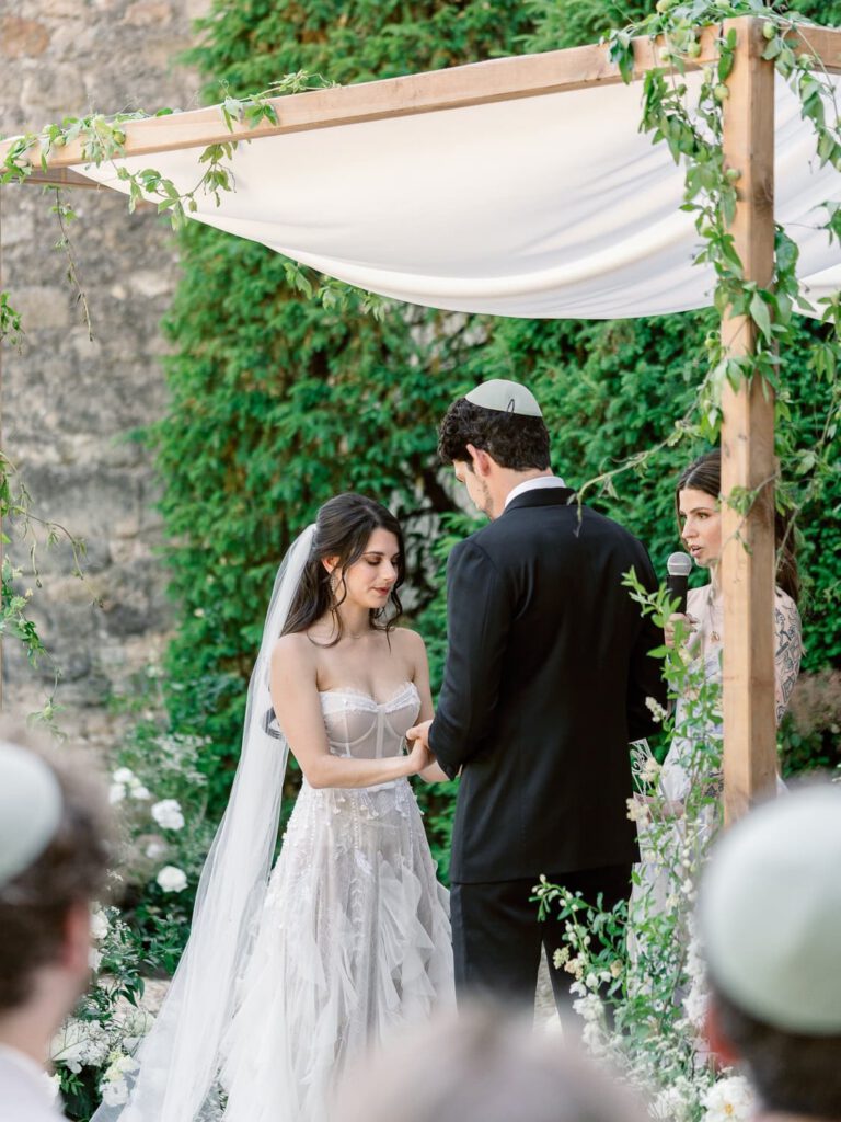 Wedding ceremony with a chuppah decorated with white flower and green foliage at Château de Fontarèches