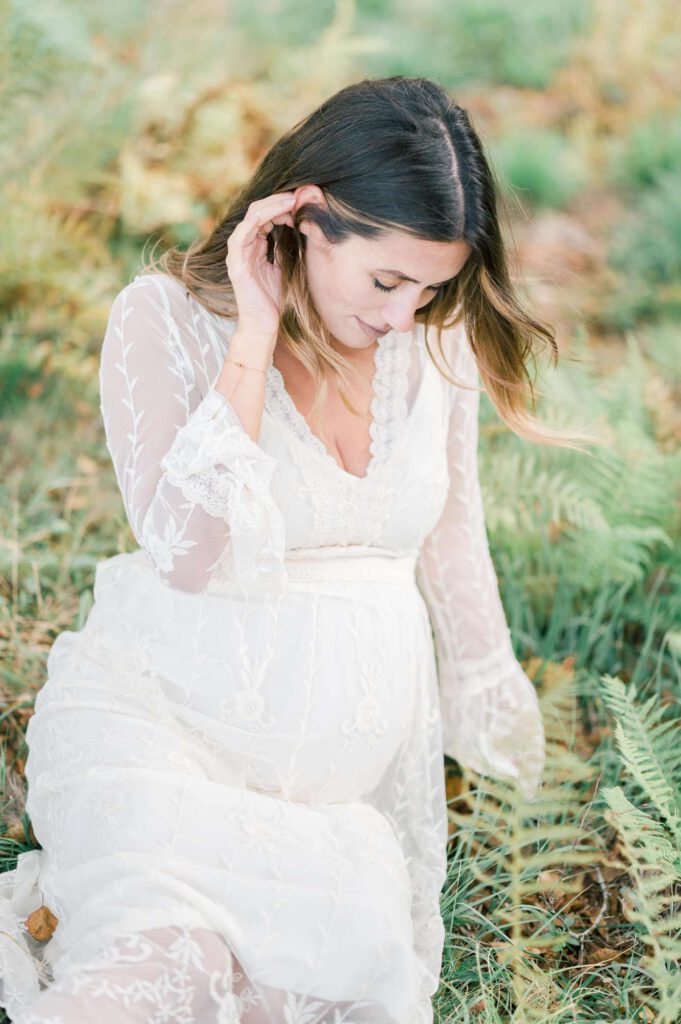 femme enceinte en robe blanche assise dans l'herbe
