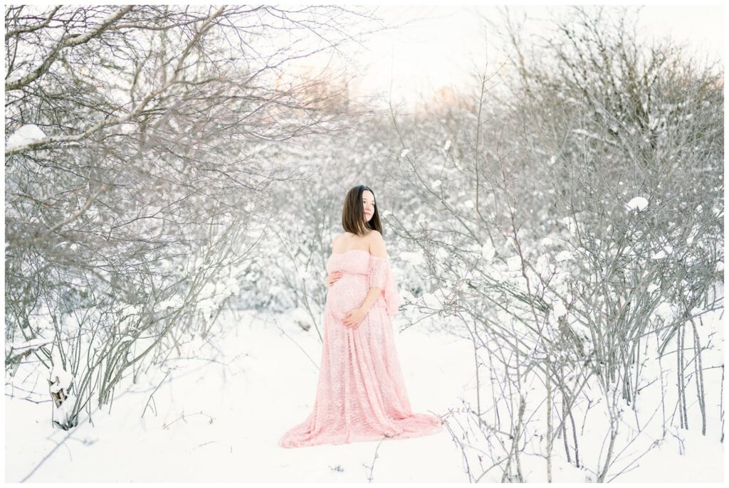 séance grossesse en hiver dans la neige avec une robe rose