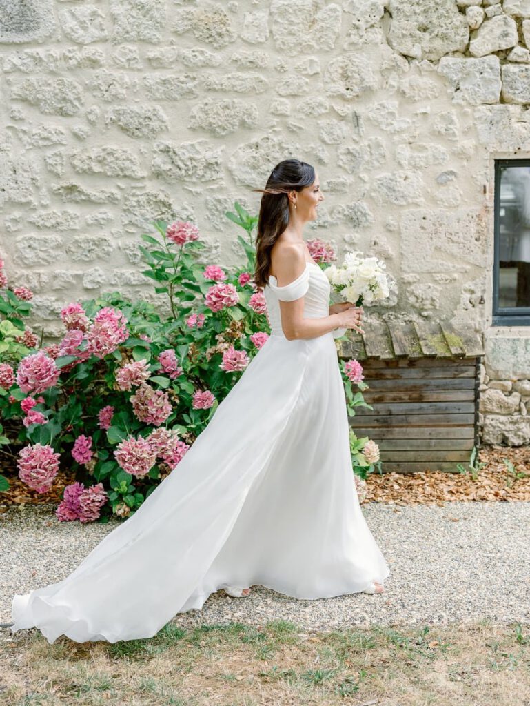 Bride in front of a stone wall and pink flowers at clos des charmes