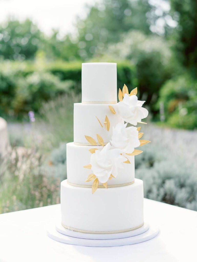 white wedding cake with white flowers and golden leaves