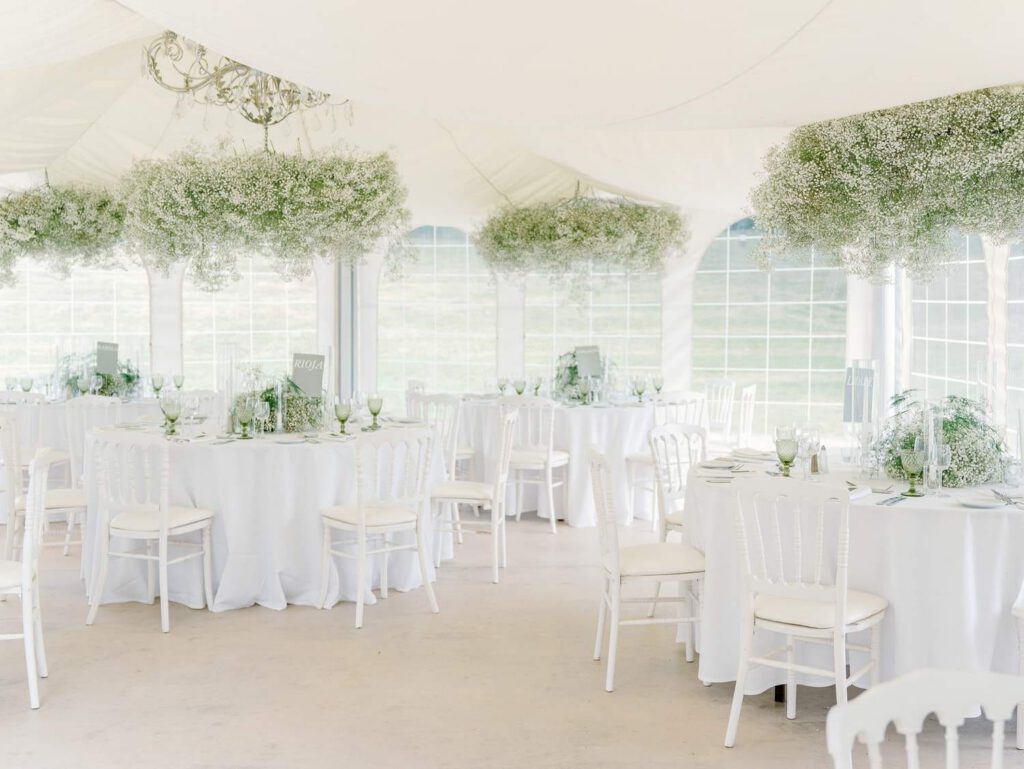 Wedding dinner tables at Domaine d'Essendieras with white chairs and tablecloth and Gypsophila flowers hanging on the ceiling