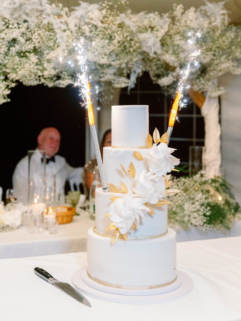 white wedding cake with white flowers and golden leaves and sparklers