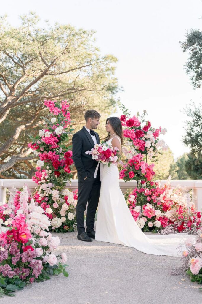 bride and groom in front of a pink arch