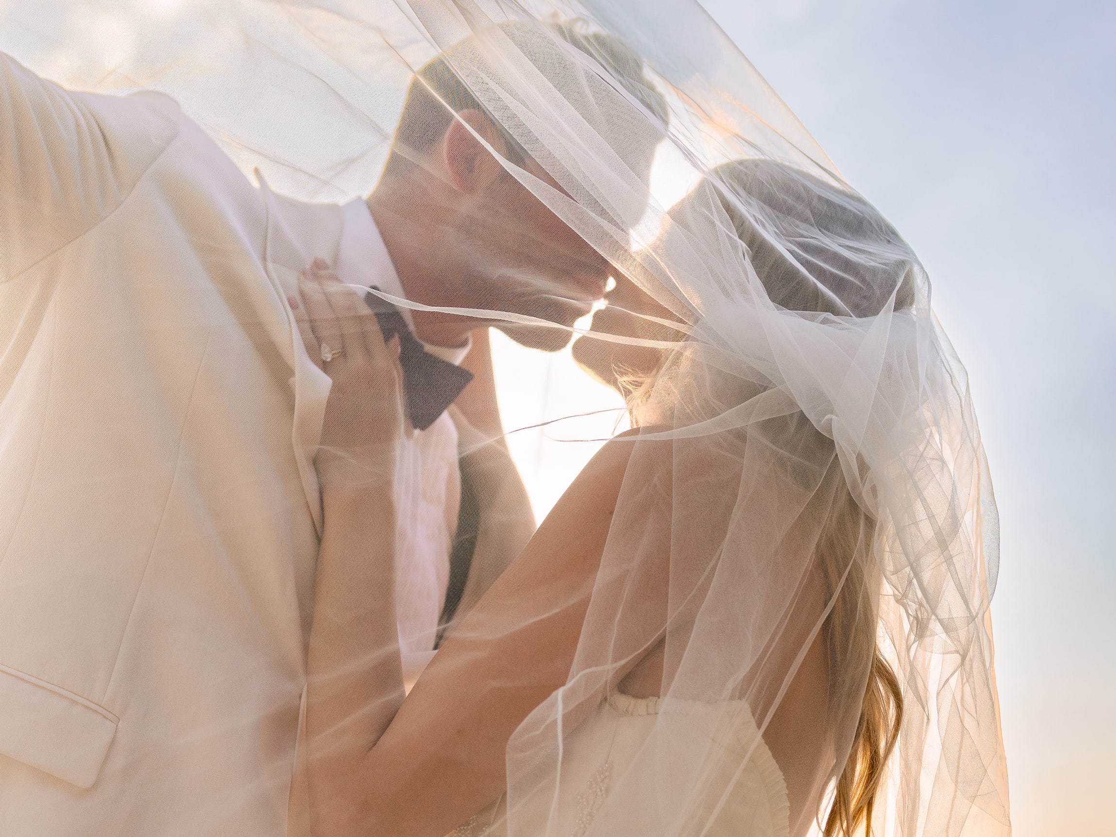 bride and groom under a veil at sunset